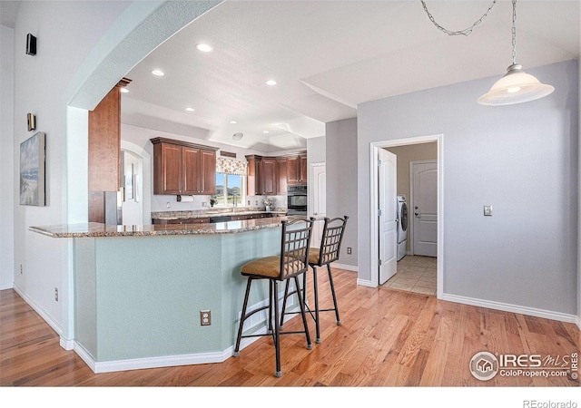kitchen featuring light stone countertops, a breakfast bar, arched walkways, a peninsula, and black oven