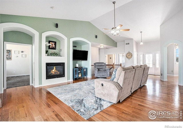 living room with wood finished floors, a ceiling fan, arched walkways, baseboards, and a glass covered fireplace