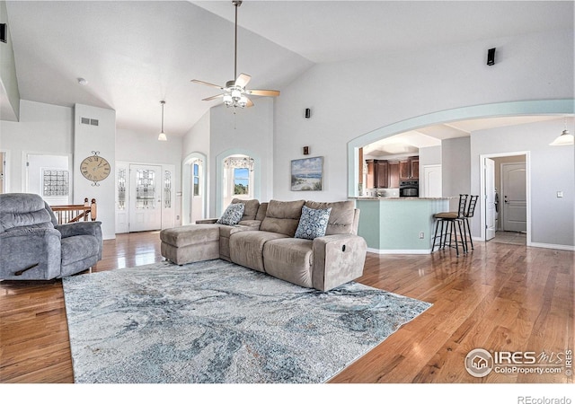 living area with high vaulted ceiling, wood finished floors, ceiling fan, arched walkways, and visible vents