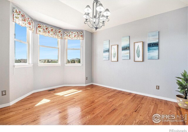 empty room featuring a wealth of natural light, a notable chandelier, light wood finished floors, and baseboards