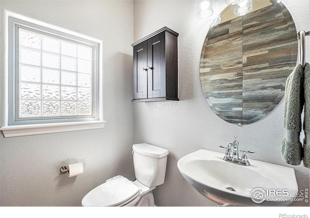 bathroom with a textured wall, a sink, and toilet