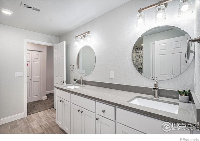 bathroom with wood finished floors, a sink, visible vents, and double vanity