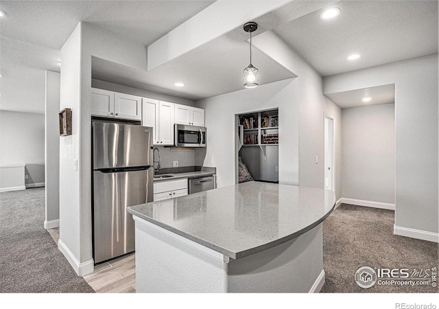 kitchen featuring white cabinets, baseboards, light colored carpet, decorative light fixtures, and appliances with stainless steel finishes