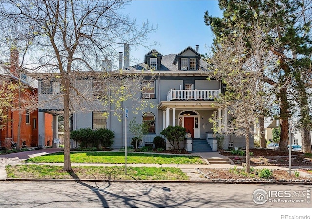 view of front of house with stucco siding, a balcony, and a front yard