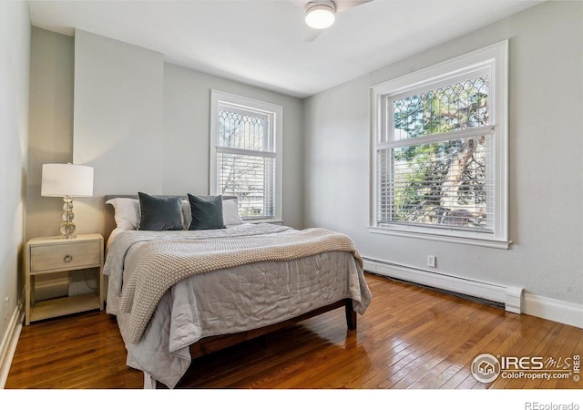 bedroom featuring a baseboard heating unit, hardwood / wood-style floors, baseboards, and multiple windows