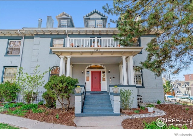 italianate home with brick siding, covered porch, and a balcony