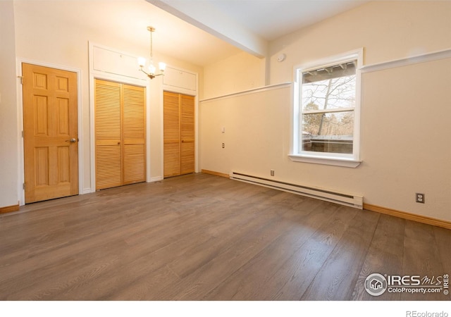 unfurnished bedroom featuring wood finished floors, baseboards, a chandelier, two closets, and baseboard heating