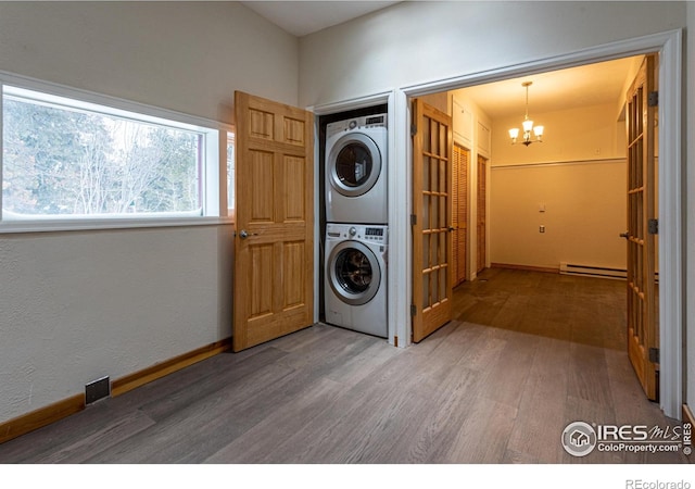 washroom featuring a baseboard radiator, stacked washer / dryer, wood finished floors, baseboards, and a chandelier
