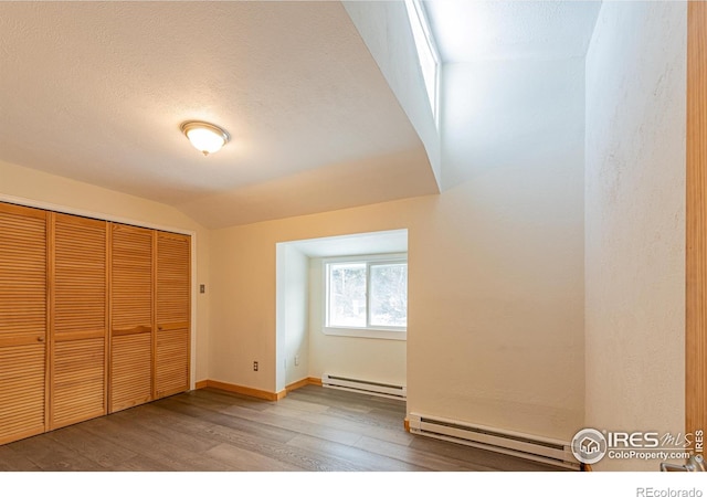 unfurnished bedroom featuring lofted ceiling, wood finished floors, a closet, and a baseboard radiator