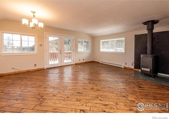 unfurnished living room featuring baseboard heating, vaulted ceiling, hardwood / wood-style floors, a wood stove, and baseboards