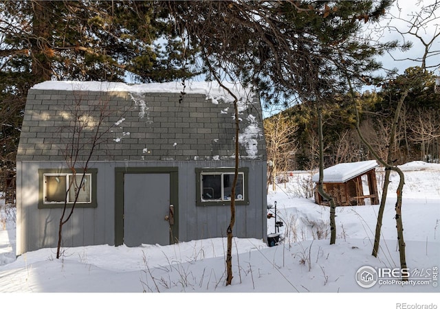 snow covered property with a gambrel roof and an outbuilding