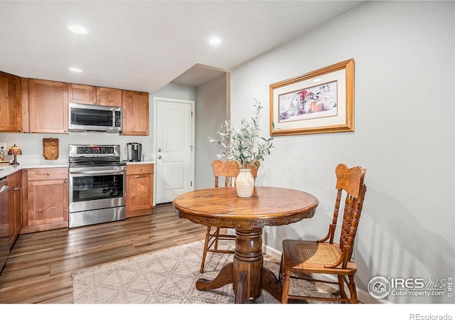 kitchen featuring recessed lighting, brown cabinets, light countertops, wood finished floors, and appliances with stainless steel finishes