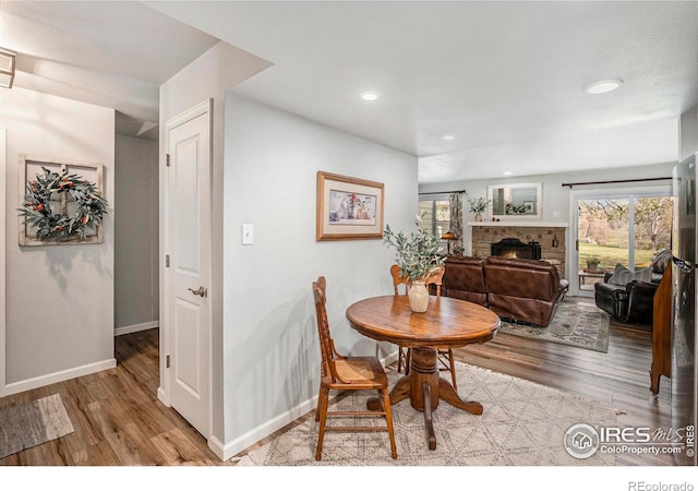 dining space featuring baseboards, wood finished floors, recessed lighting, and a warm lit fireplace