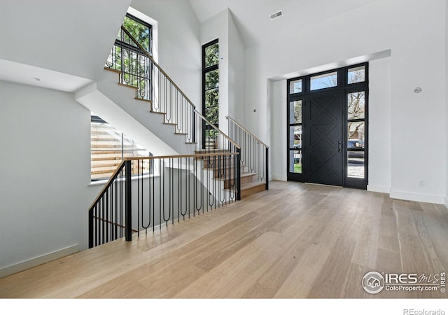 foyer entrance with wood finished floors, visible vents, baseboards, a towering ceiling, and stairway