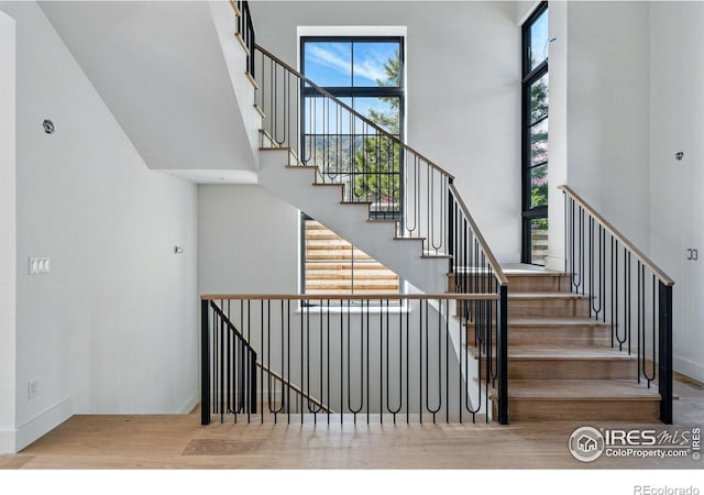 stairs with baseboards, wood finished floors, and a towering ceiling