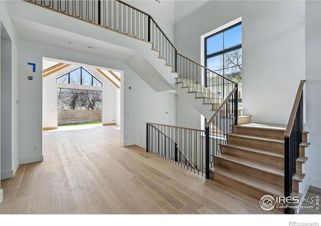 stairs with a wealth of natural light, wood finished floors, and a towering ceiling