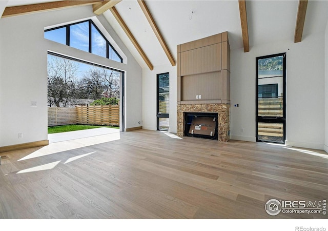 unfurnished living room featuring a fireplace with flush hearth, a wealth of natural light, light wood-style flooring, and beamed ceiling