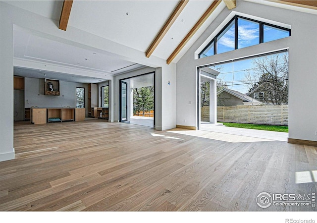 unfurnished living room with wood finished floors, baseboards, high vaulted ceiling, and beam ceiling