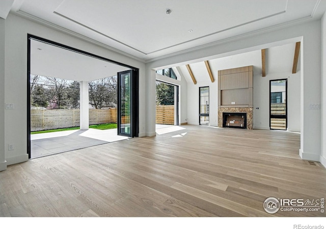 unfurnished living room with light wood-style flooring, lofted ceiling with beams, baseboards, and a high end fireplace