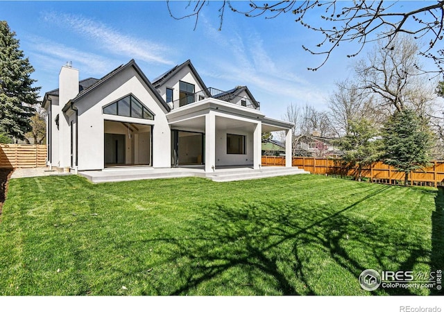 back of property featuring a chimney, a fenced backyard, a balcony, a yard, and a patio area