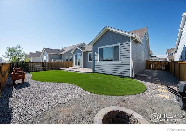 back of house featuring a fenced backyard, a fire pit, a lawn, and a patio area