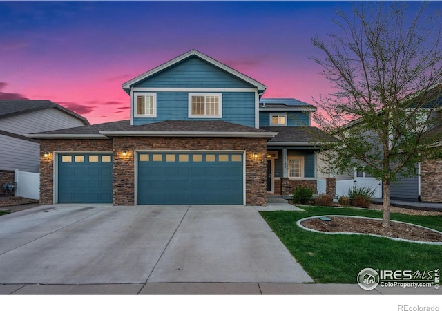 traditional home featuring an attached garage, stone siding, concrete driveway, and a lawn