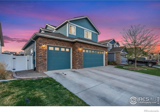 view of front of property with a gate, stone siding, concrete driveway, fence, and an attached garage