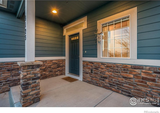 doorway to property with a porch and stone siding