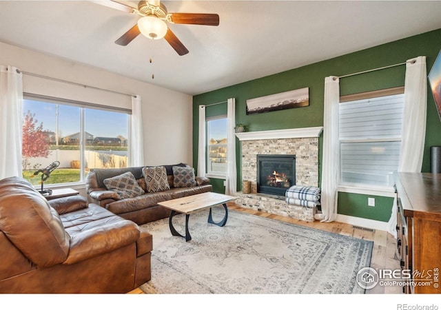 living area with baseboards, a ceiling fan, wood finished floors, and a stone fireplace