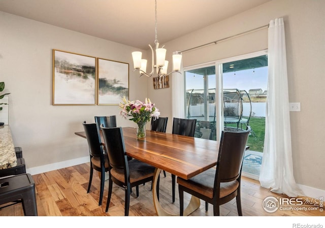 dining area with light wood-style flooring, baseboards, and a notable chandelier