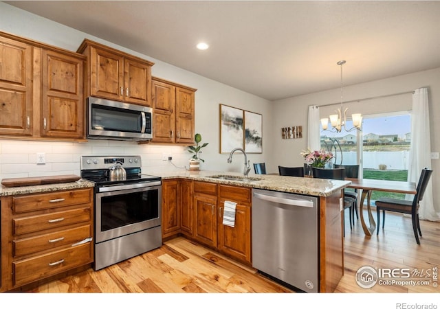 kitchen with a peninsula, a sink, light wood-type flooring, brown cabinetry, and appliances with stainless steel finishes
