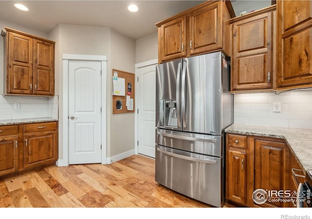 kitchen with brown cabinets, decorative backsplash, light wood-style flooring, stainless steel refrigerator with ice dispenser, and recessed lighting