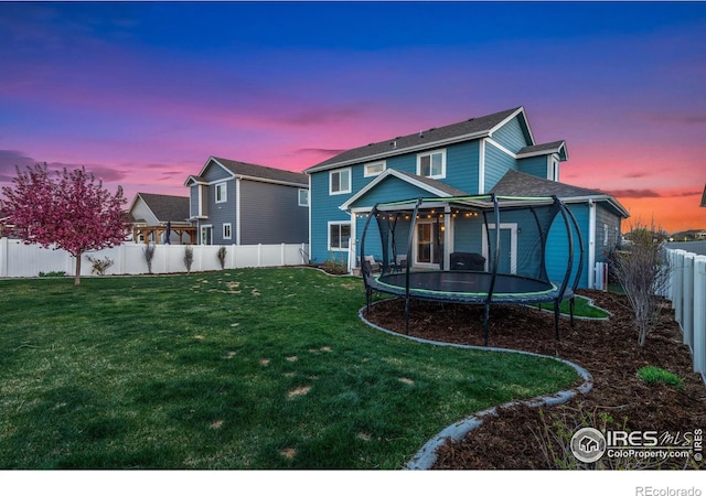 rear view of house with a lawn, a fenced backyard, and a trampoline