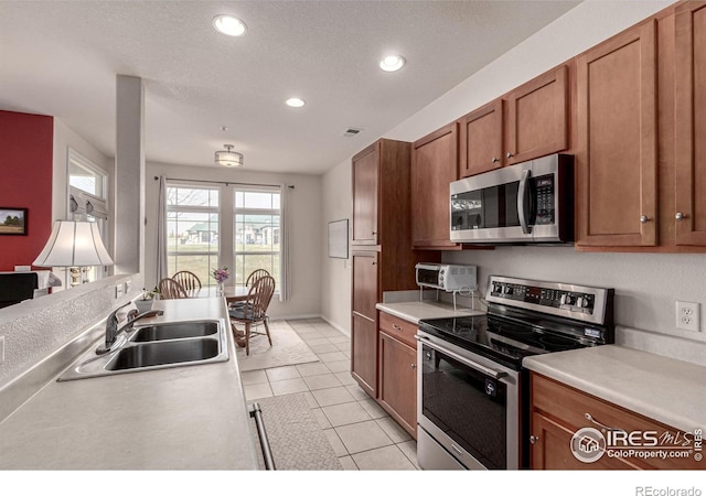 kitchen with recessed lighting, light countertops, a sink, brown cabinetry, and appliances with stainless steel finishes