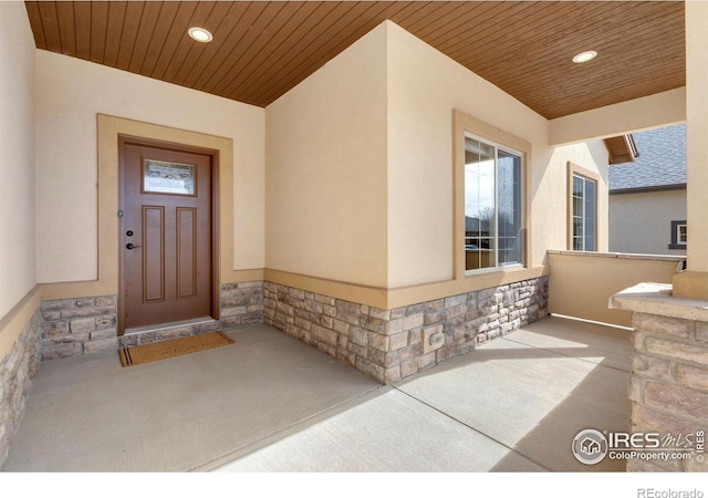 property entrance featuring stone siding, a shingled roof, and stucco siding