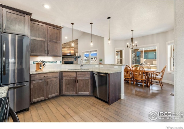 kitchen with a peninsula, light wood-style flooring, a sink, decorative backsplash, and appliances with stainless steel finishes