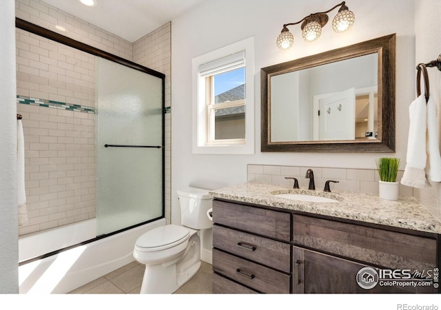 bathroom featuring tile patterned flooring, combined bath / shower with glass door, toilet, and vanity
