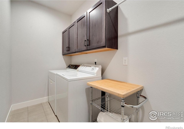 clothes washing area featuring cabinet space, baseboards, washer and dryer, and light tile patterned floors