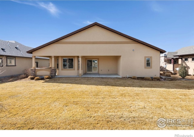 rear view of property with stucco siding, a patio, and a lawn