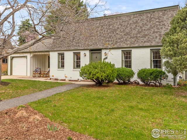view of front of house featuring driveway, an attached garage, a front yard, brick siding, and roof with shingles