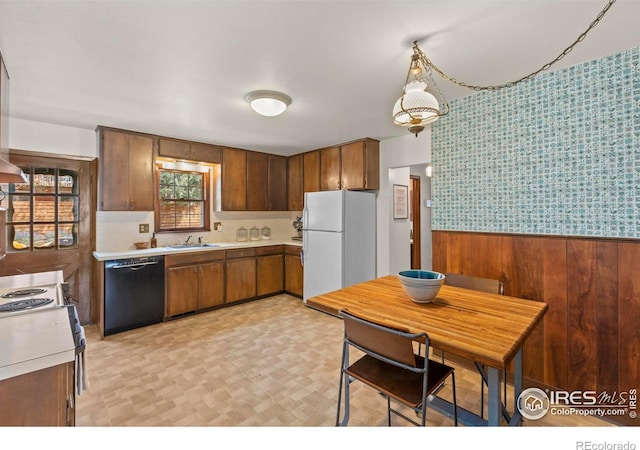 kitchen featuring a sink, wallpapered walls, light countertops, black dishwasher, and freestanding refrigerator