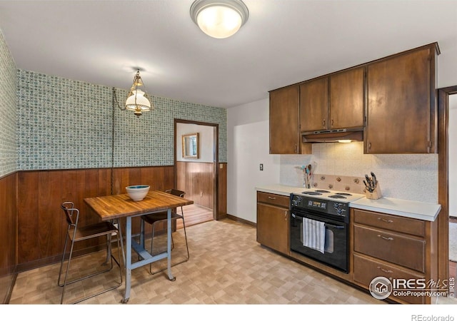 kitchen with wallpapered walls, wainscoting, black electric range, light countertops, and under cabinet range hood