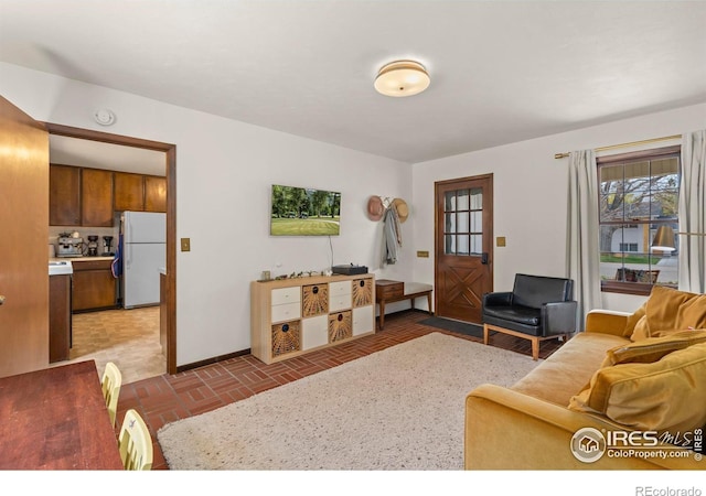 living area with baseboards and brick floor