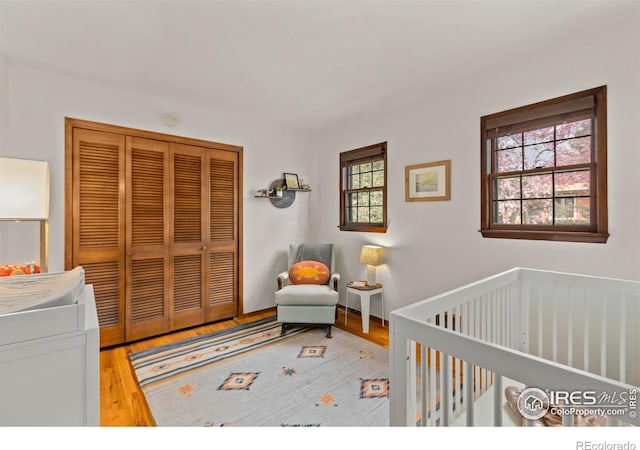 bedroom with a nursery area, wood finished floors, and a closet
