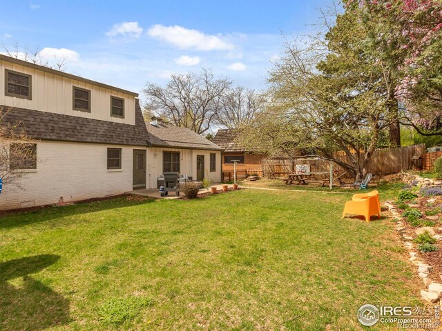 rear view of property with a lawn, a shingled roof, fence, a patio, and brick siding