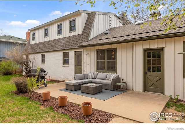 back of property featuring a shingled roof, board and batten siding, a patio, an outdoor living space, and brick siding