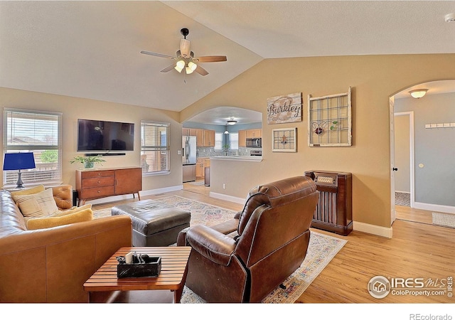 living area featuring a ceiling fan, a wealth of natural light, arched walkways, light wood finished floors, and lofted ceiling