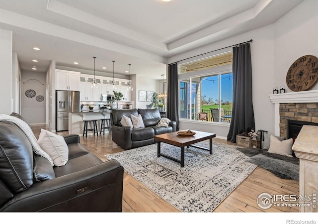 living room with recessed lighting, a raised ceiling, and light wood-type flooring