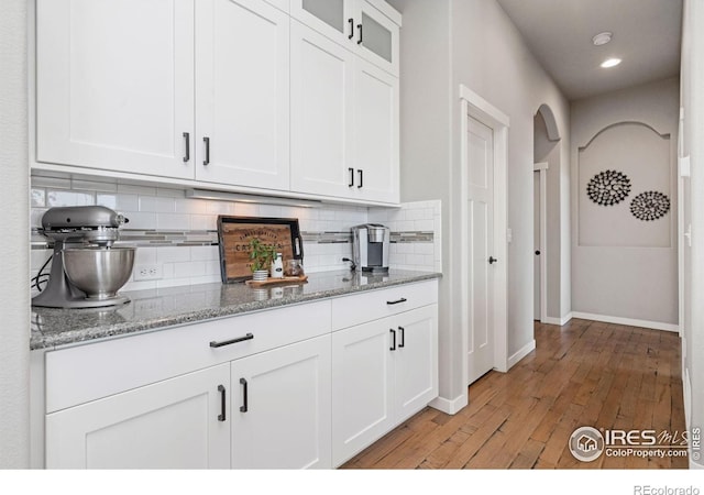 bar featuring arched walkways, tasteful backsplash, light wood-type flooring, baseboards, and recessed lighting