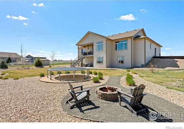 rear view of house featuring a fire pit, a trampoline, a patio area, a lawn, and stairs